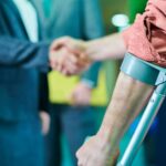 A man with crutches shaking hands with a lawyer regarding legal support in accident claims
